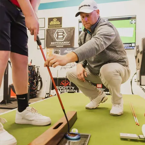 Coach teaching junior golfer at indoor green